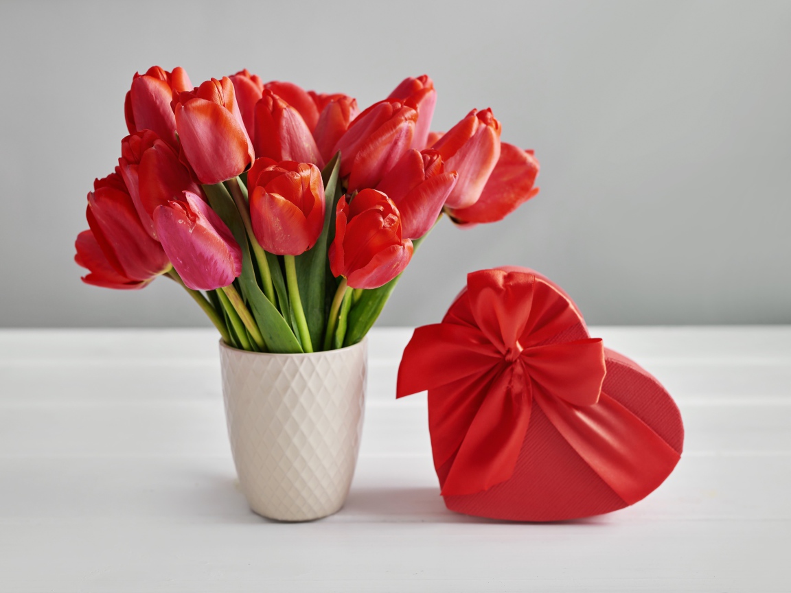 Bouquet of red tulips on a table with a heart-shaped box