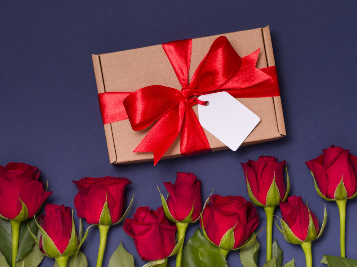 Подарок с красным бантом на столе с розами