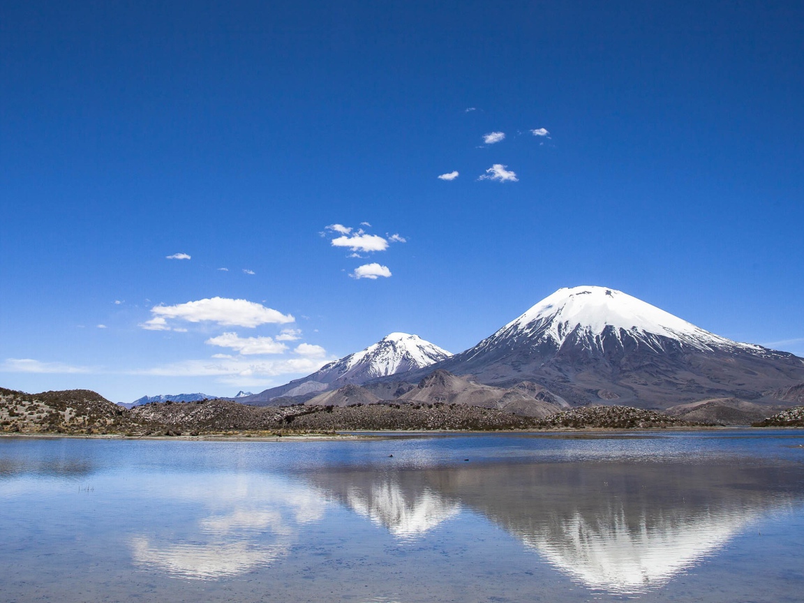 Заснеженные вершины гор под голубым небом отражаются в воде 