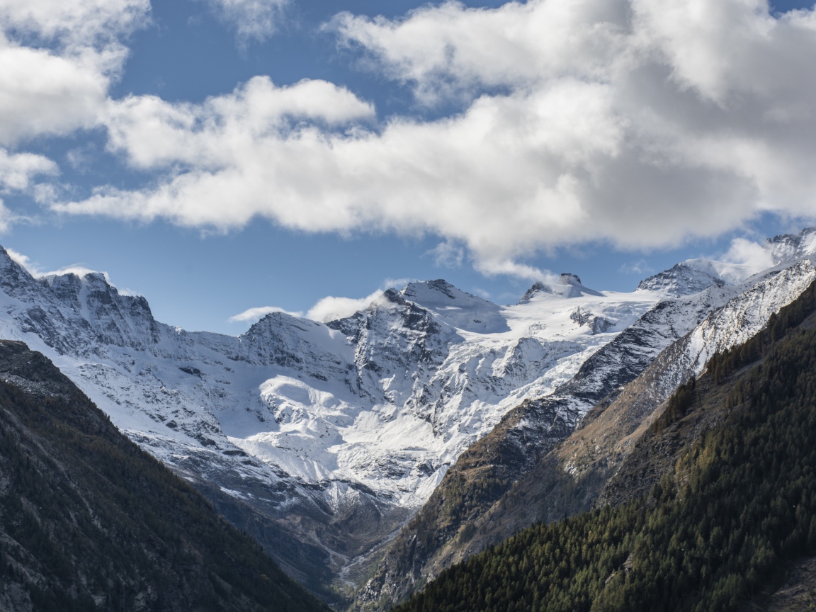 Заснеженные горы под голубым небом с белыми облаками