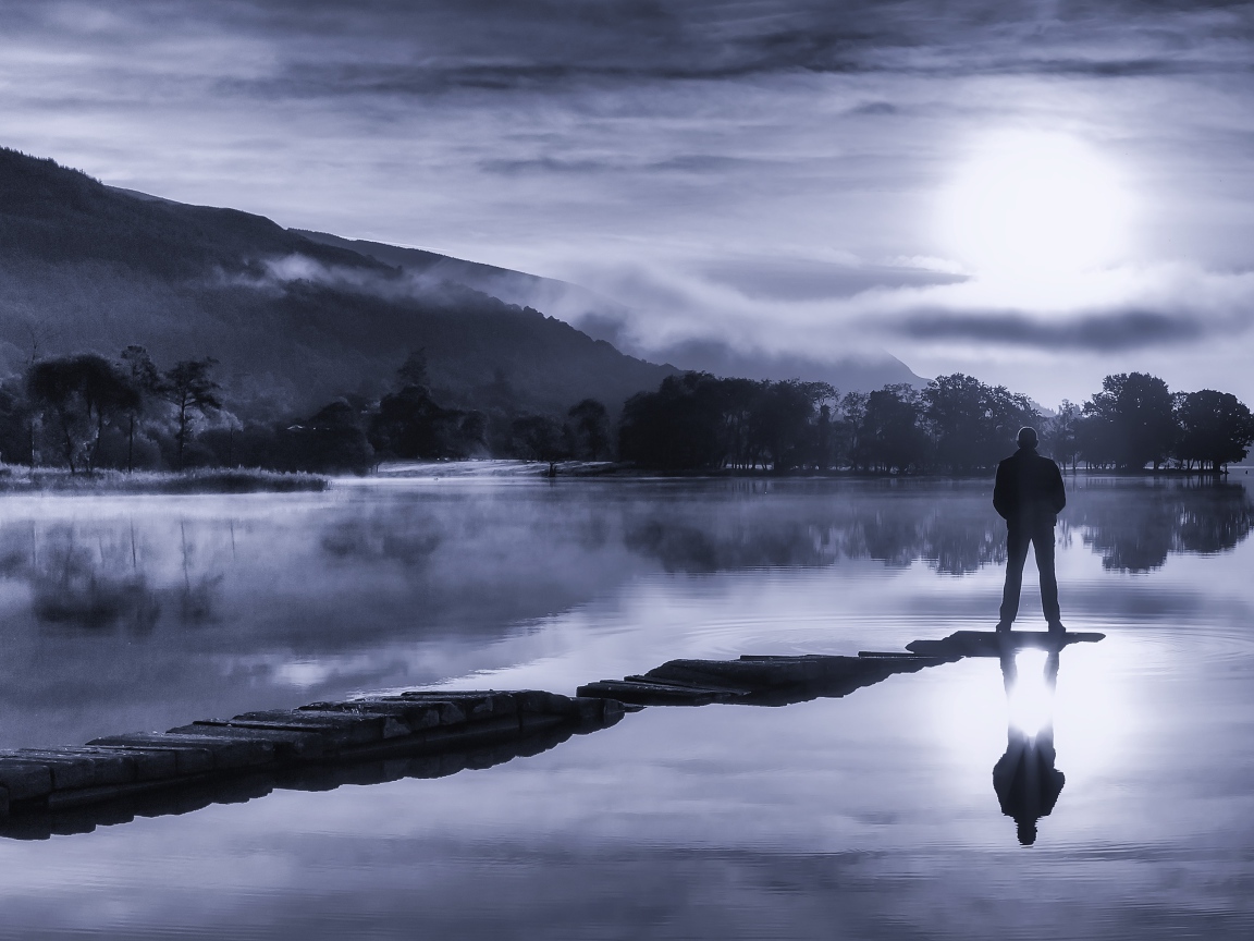 Мужчина стоит на мосту у озера ночью при свете луны