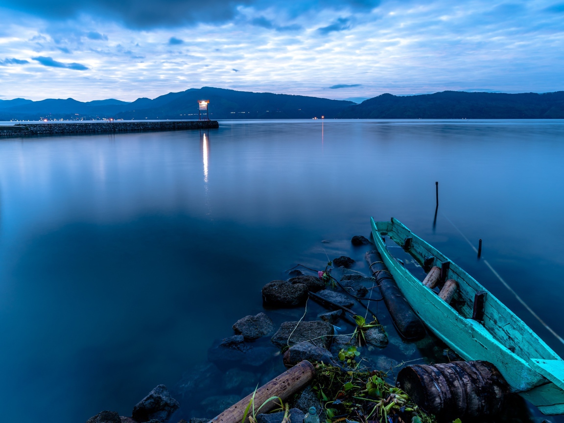 Деревянная лодка на берегу тихого озера в сумерках 