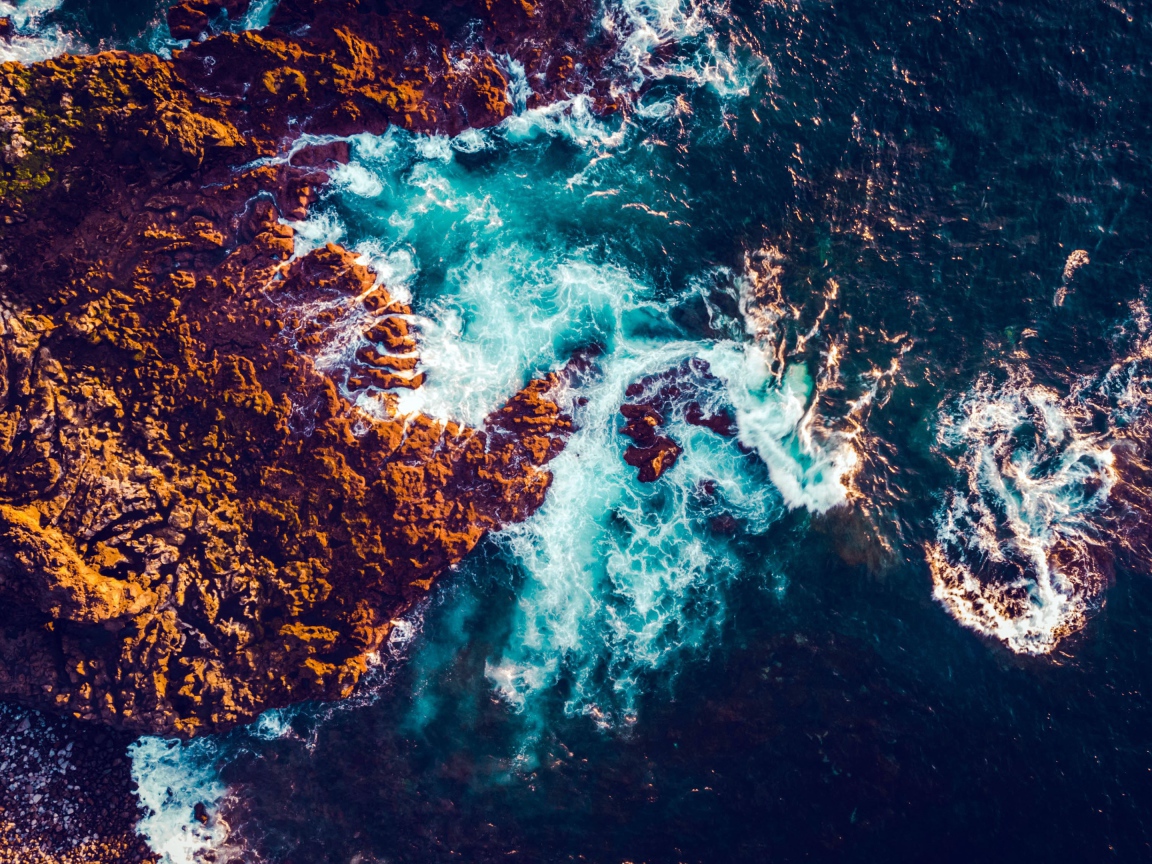 Белые морские волны бьются об камни, вид сверху