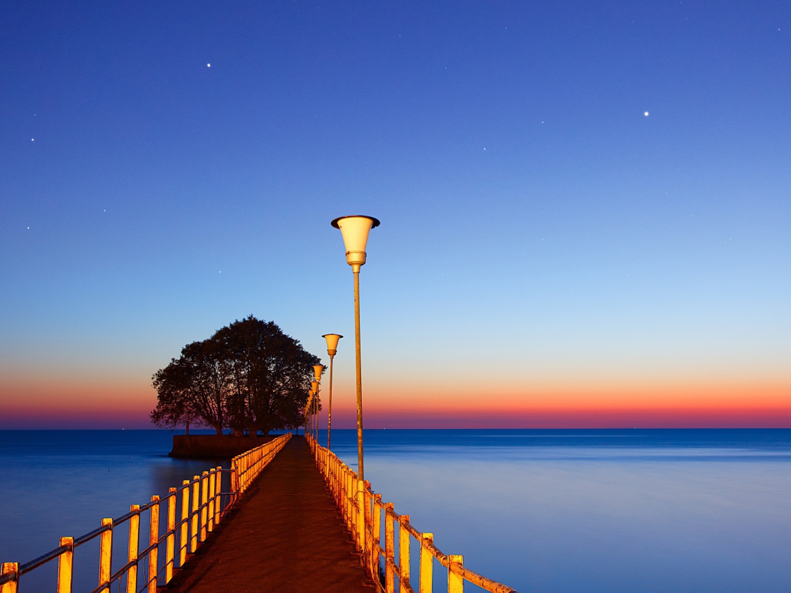 Мост в фонарями в море на закате 