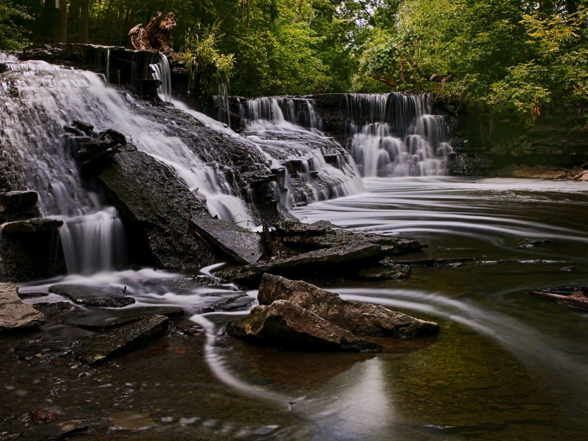 Быстрая вода стекает по камням водопада в парке 