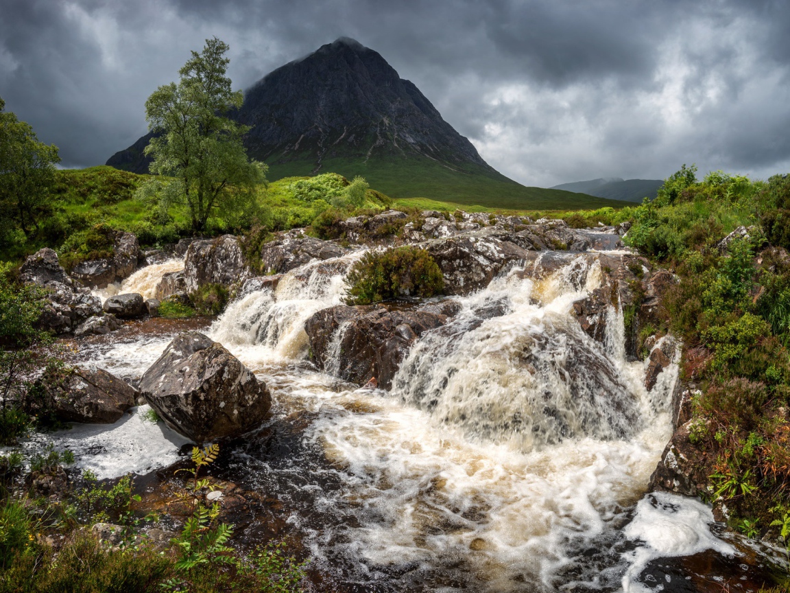 Водопад стекает по камням у горы на фоне грозового неба