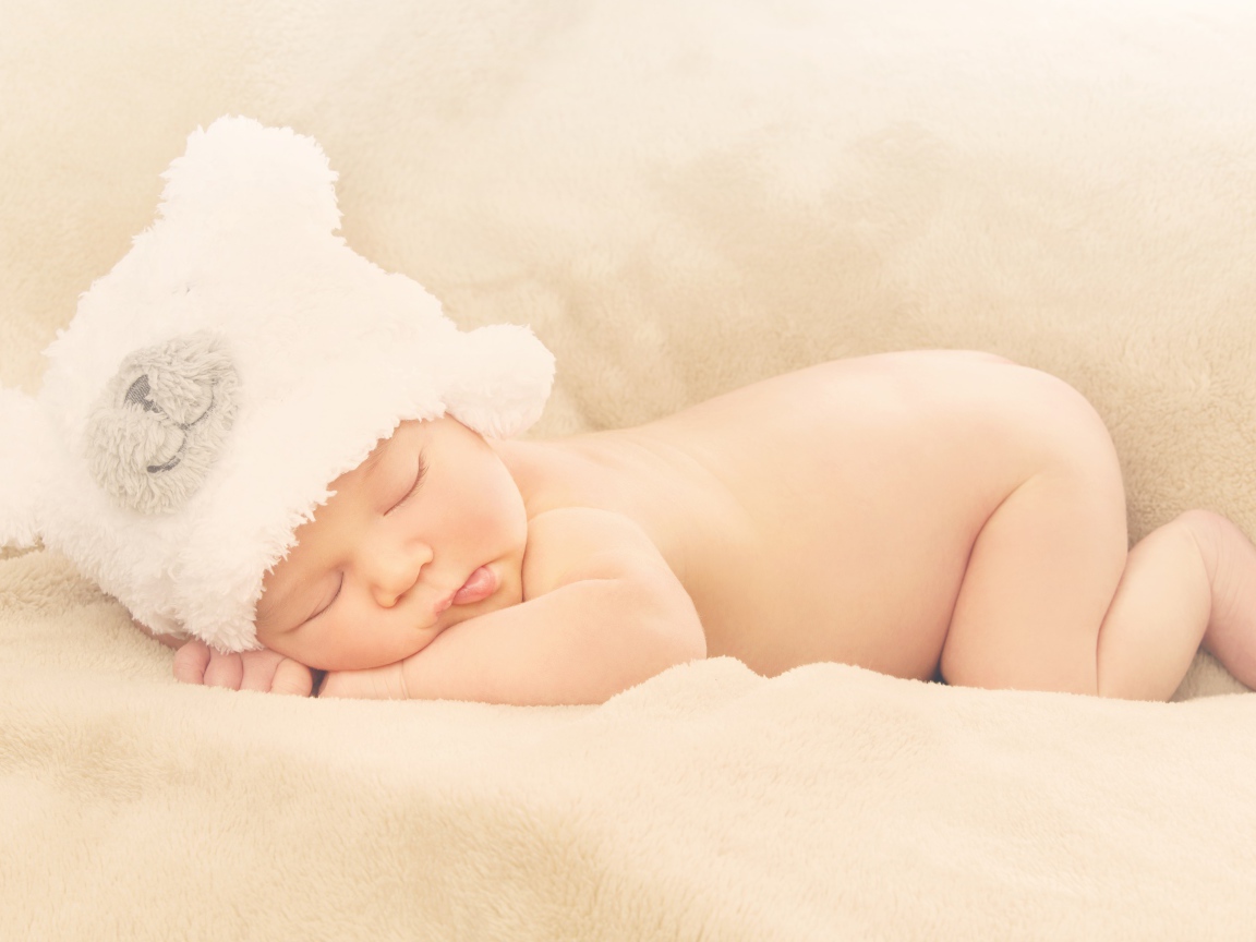 Грудной ребенок с белой шапке спит на кровати