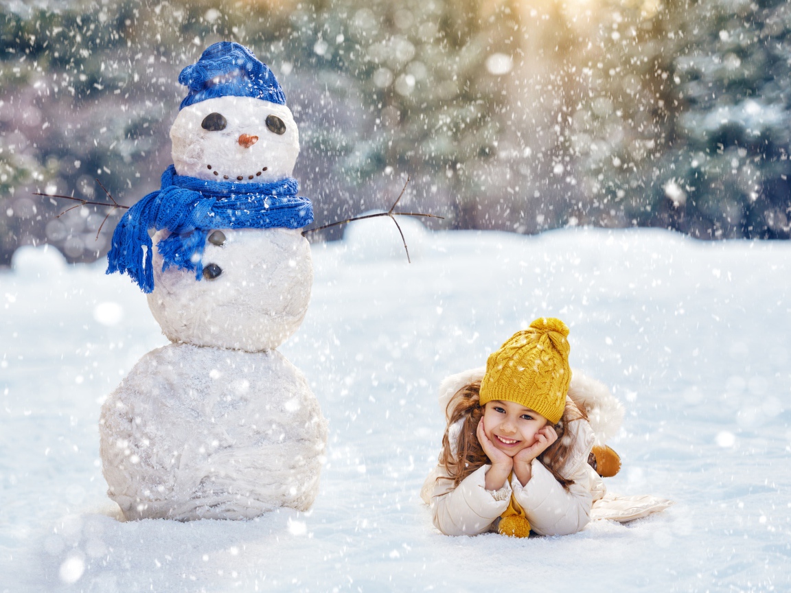 Милая девочка лежит на снегу у снеговика зимой