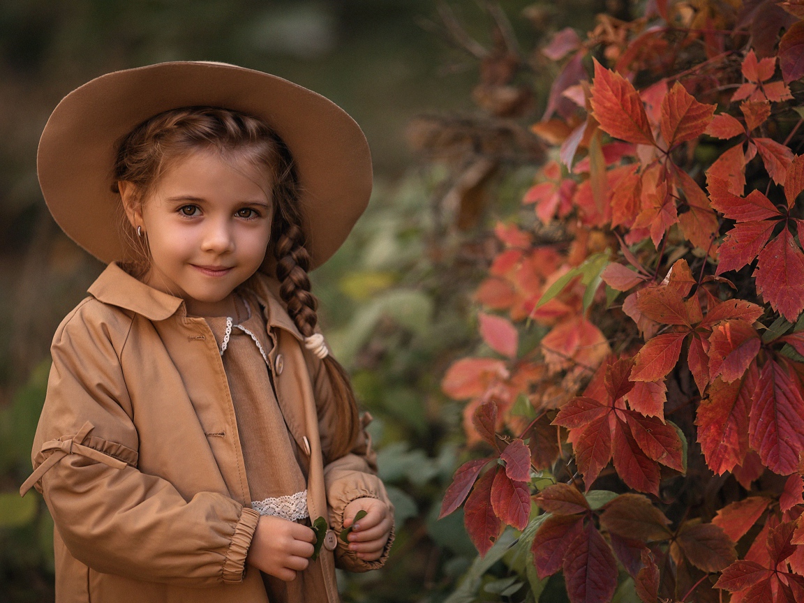 Красивая девочка шляпе стоит у дикого винограда 