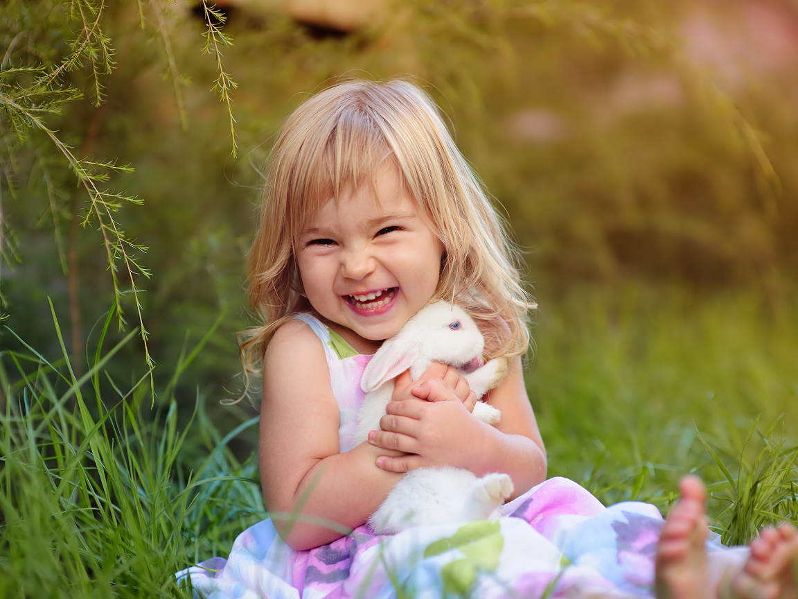 Довольная маленькая девочка обнимает белого кролика на траве 