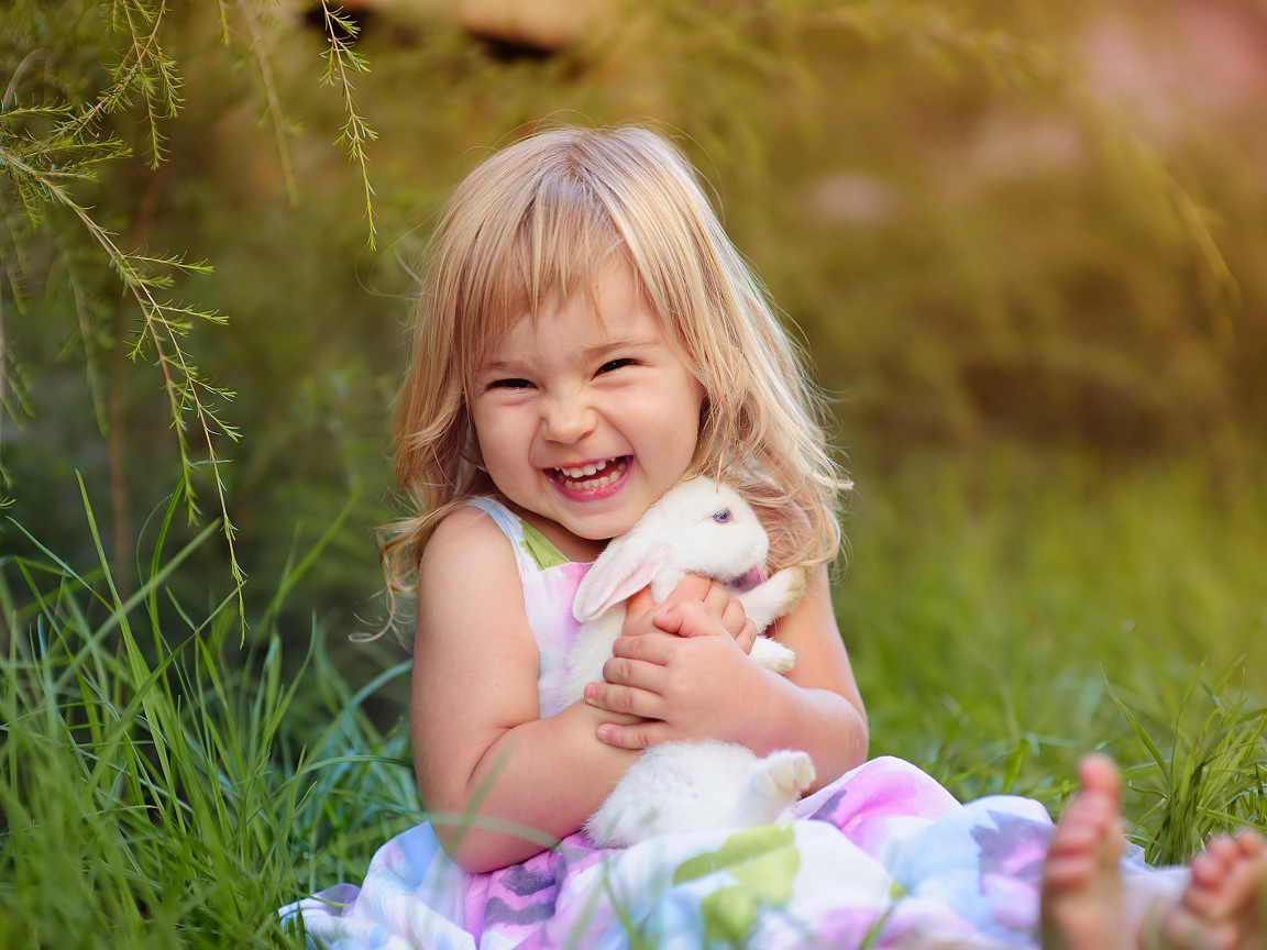 Довольная маленькая девочка обнимает белого кролика на траве 