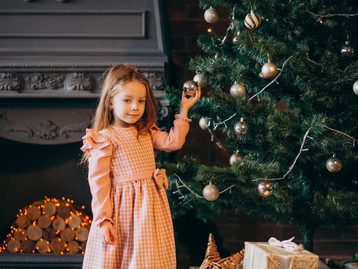 Милая маленькая девочка стоит у наряженной елки 