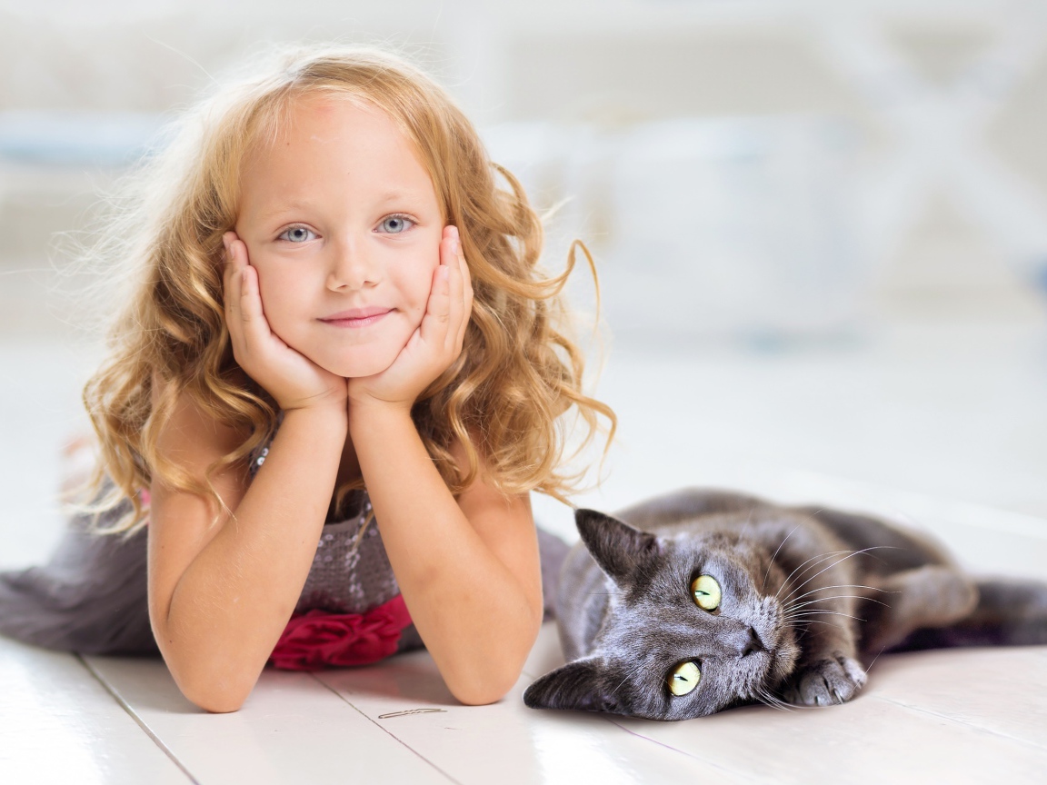 Маленькая милая голубоглазая девочка лежит на полу с котом