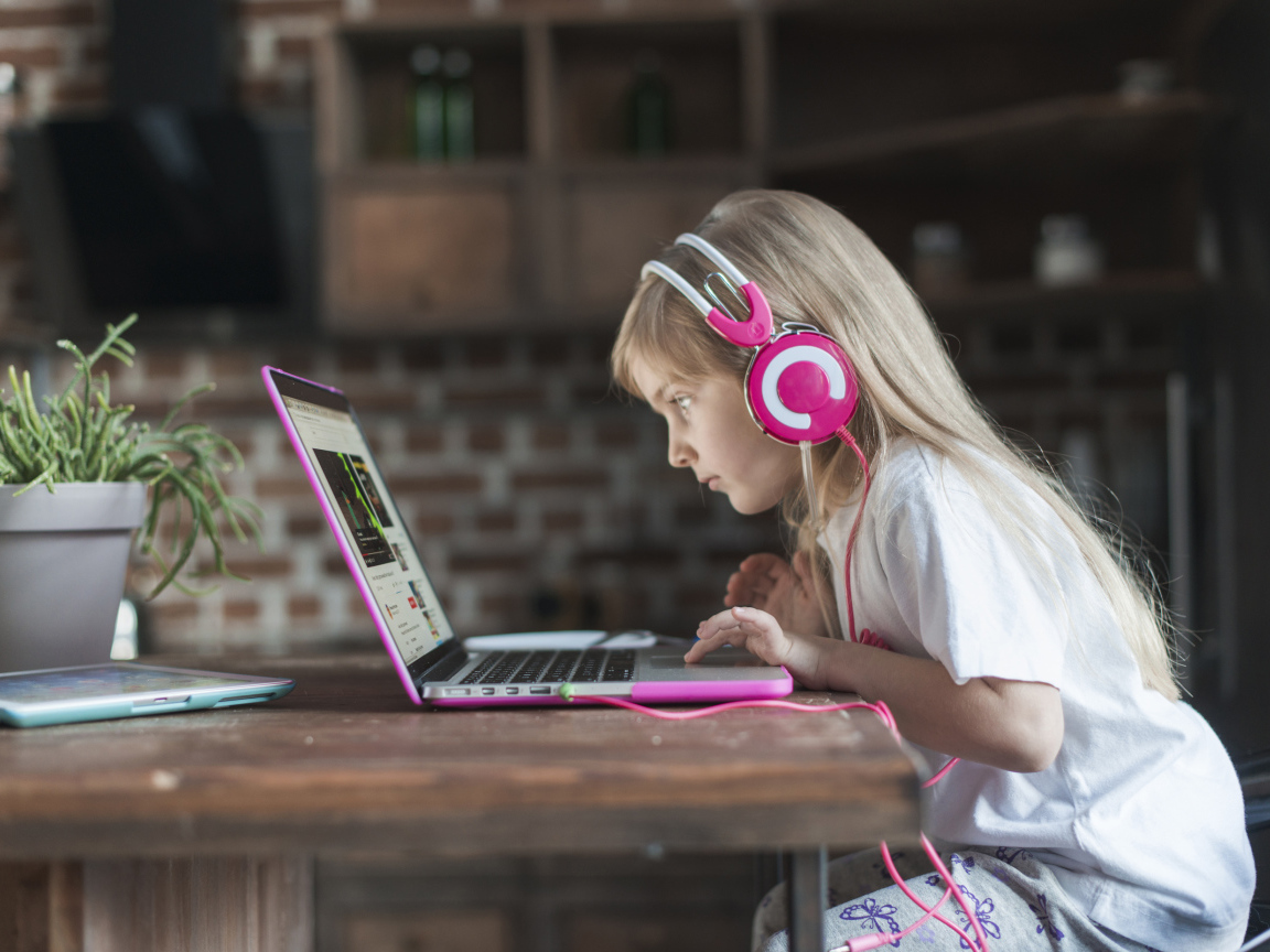 Маленькая девочка в наушниках сидит за ноутбуком