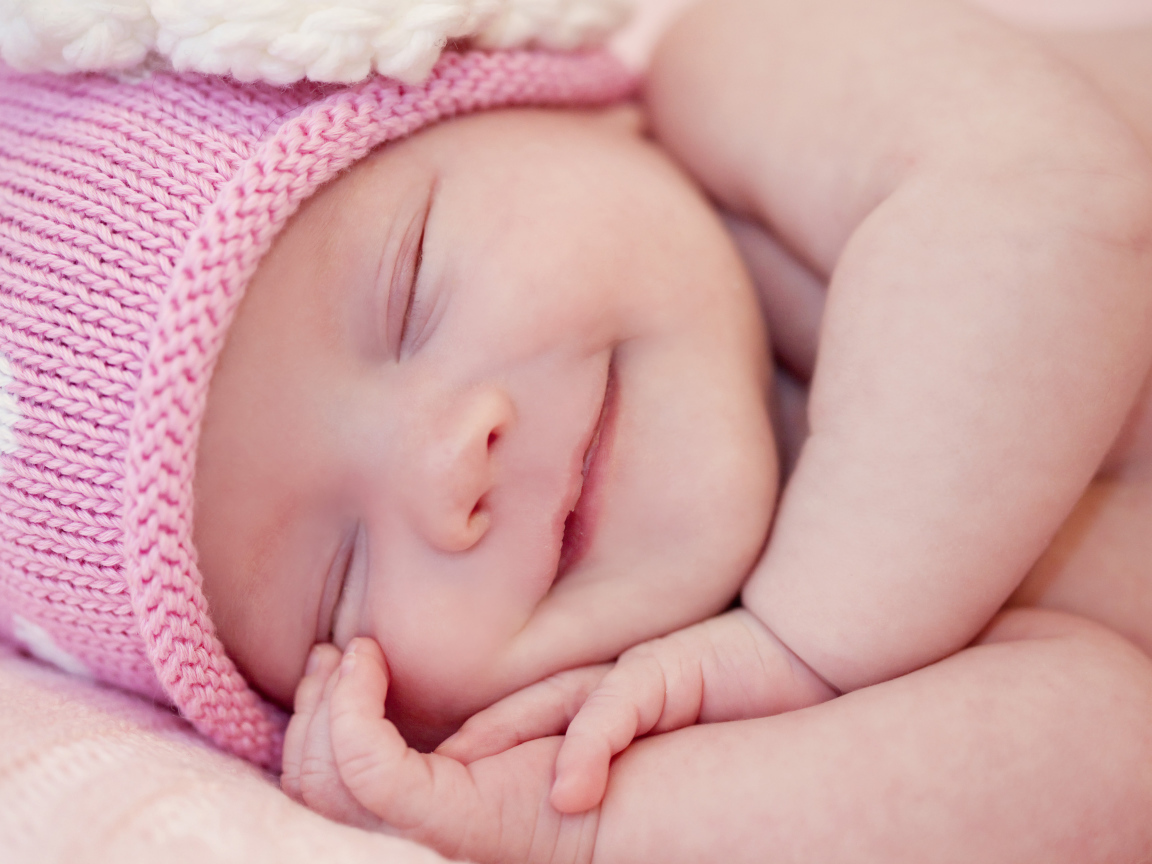 Улыбающийся грудной ребенок в розовой вязаной шапке 