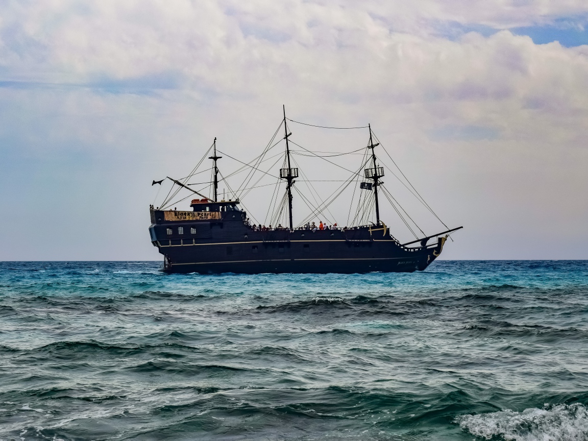 Большой черный пиратский корабль с опущенными парусами в море 