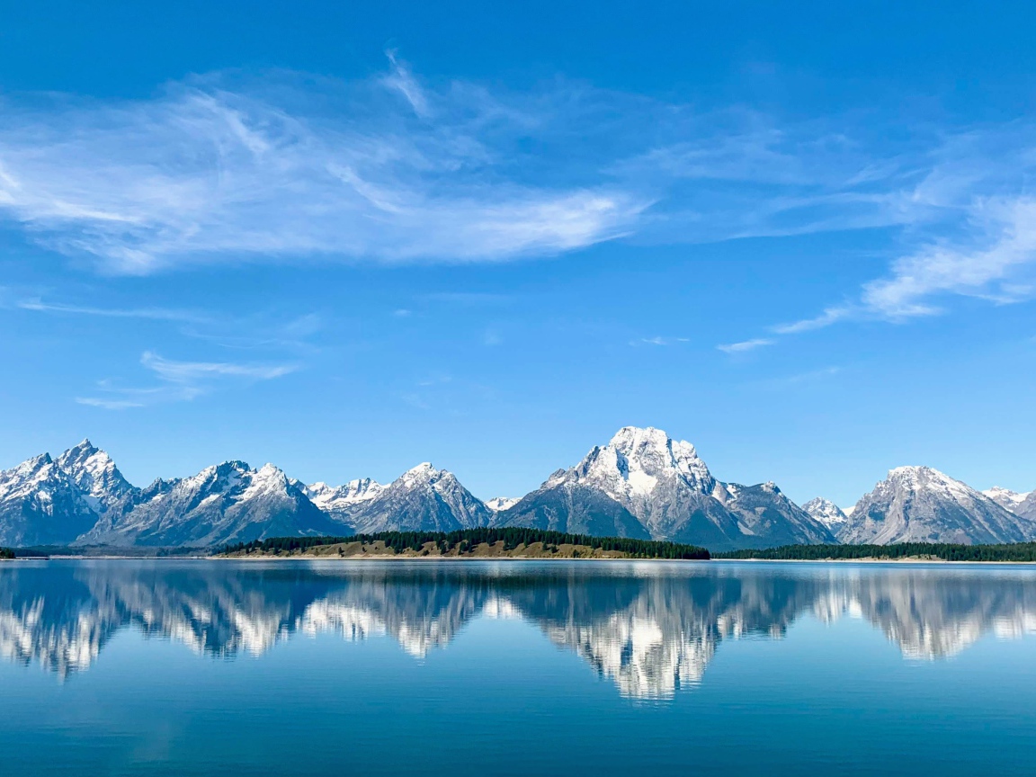 Вид на заснеженные горы под голубым небом у озера, Национальный парк Гранд Титон, Вайоминг. США
