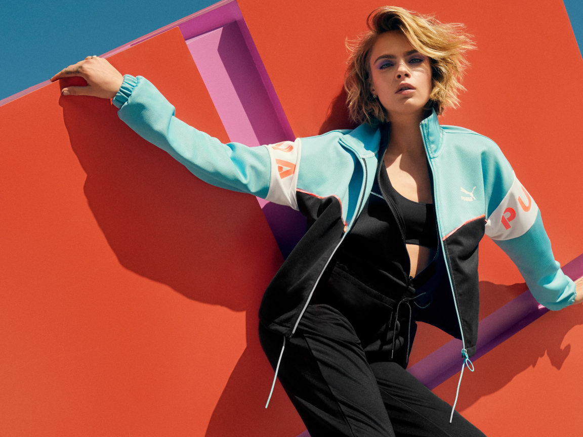 Красивая актриса Кара Делевинь в спортивном костюме у стены 