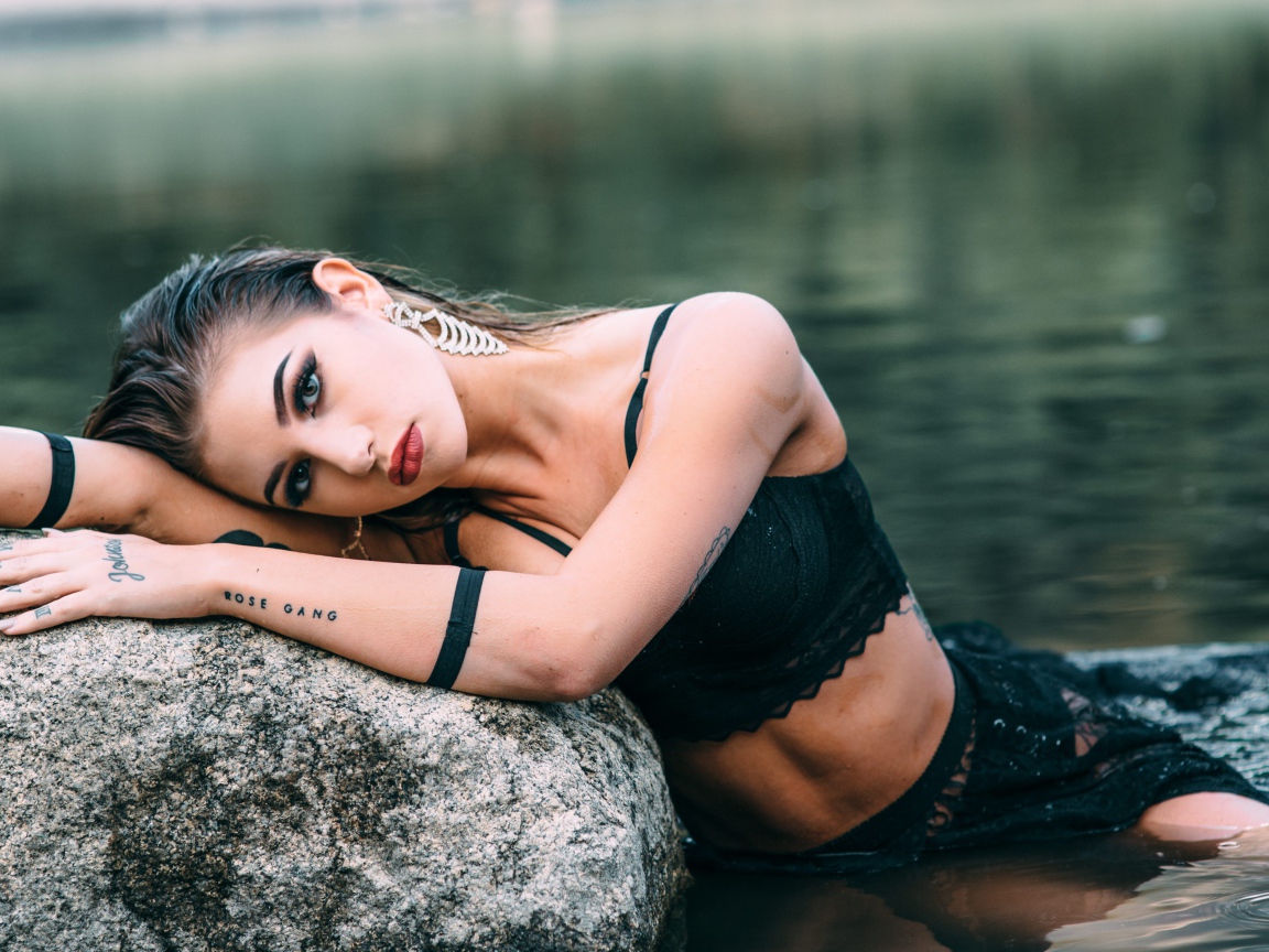 Красивая девушка в черном наряде с татуировками на руках 