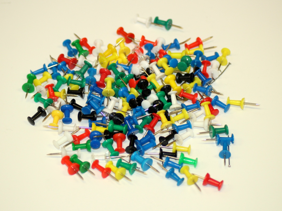 Разноцветные канцелярские гвозди на белом фоне