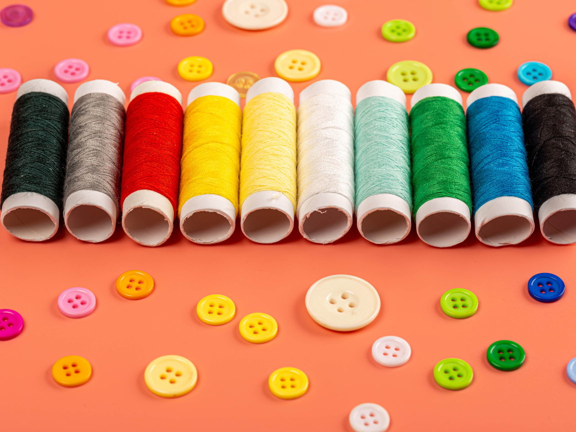 Разноцветные нитки и пуговицы на розовом фоне