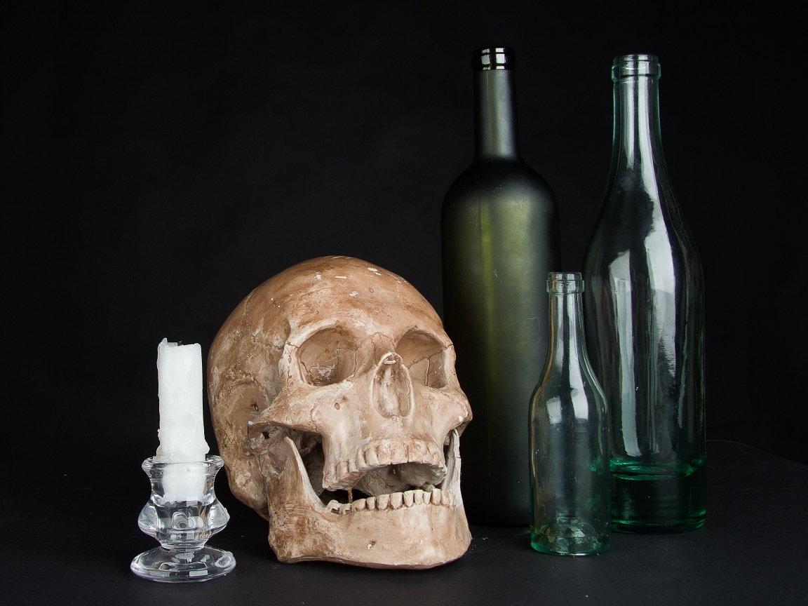 Череп, пустые бутылки и свеча на черном фоне