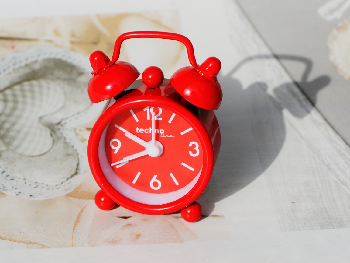 Маленький красный будильник стоит на столе 