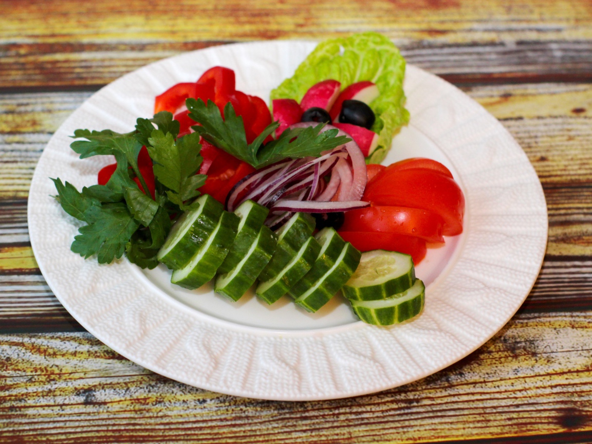 Свежие овощи на белой тарелке на деревянном фоне