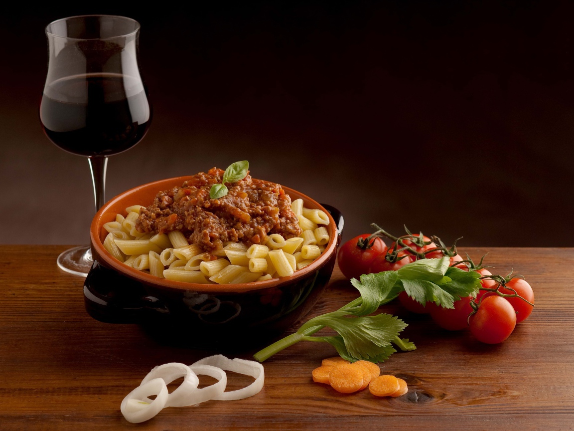 Макароны с фаршем на столе с бокалом вина и помидорами