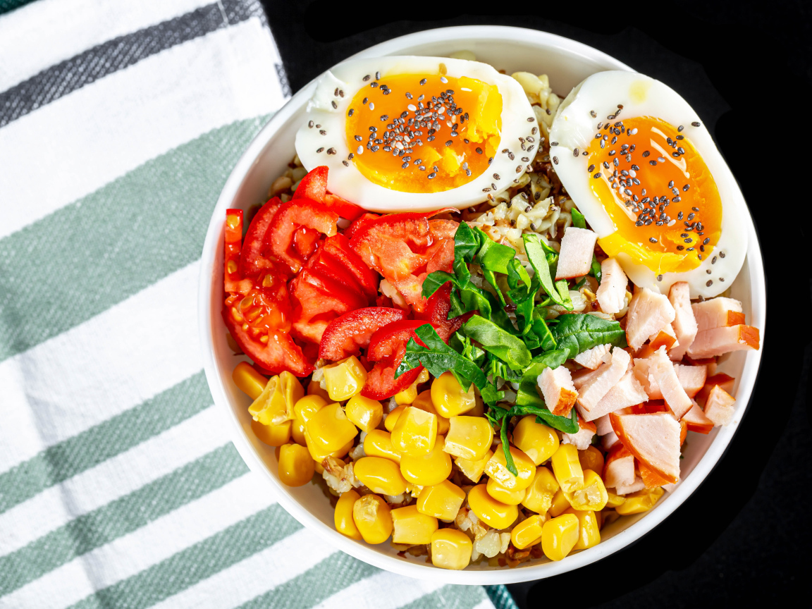 Каша в тарелке с помидорами, кукурузой, ветчиной и яйцом