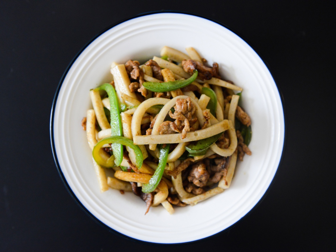 Салат с мясом в белой тарелке на черном фоне