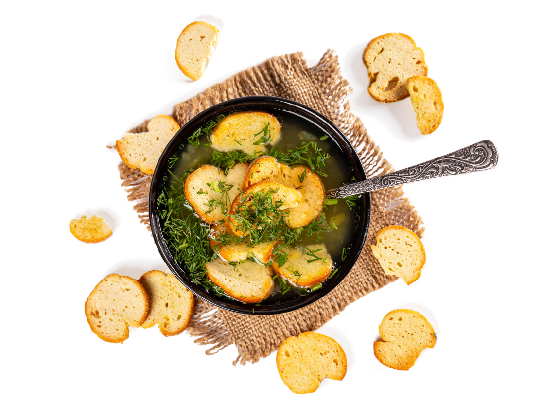 Суп с гренками и зеленью на столе на белом фоне