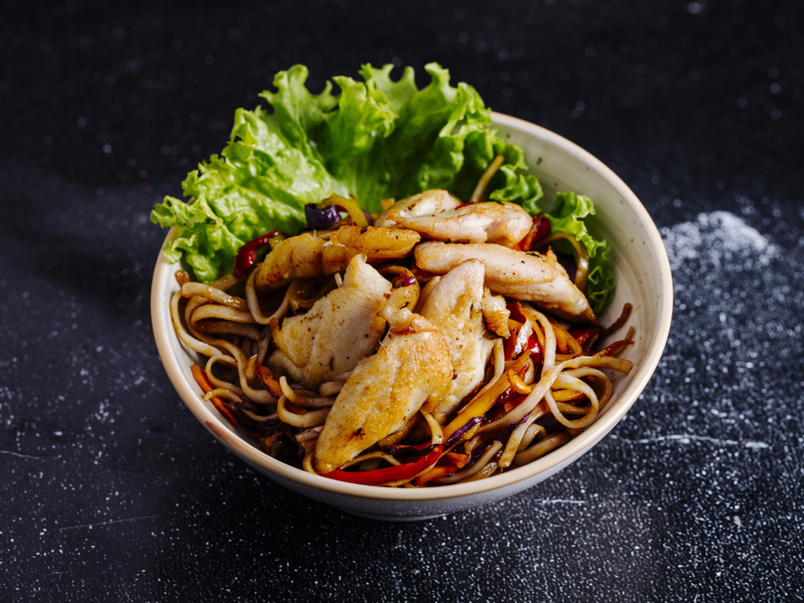 Спагетти с соусом в тарелке с кусочками курицы и листьями салата