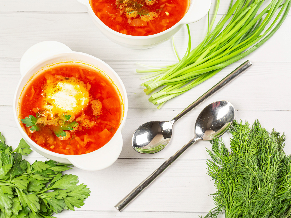 Две тарелки борща на столе с зеленью петрушки, луком и укропом