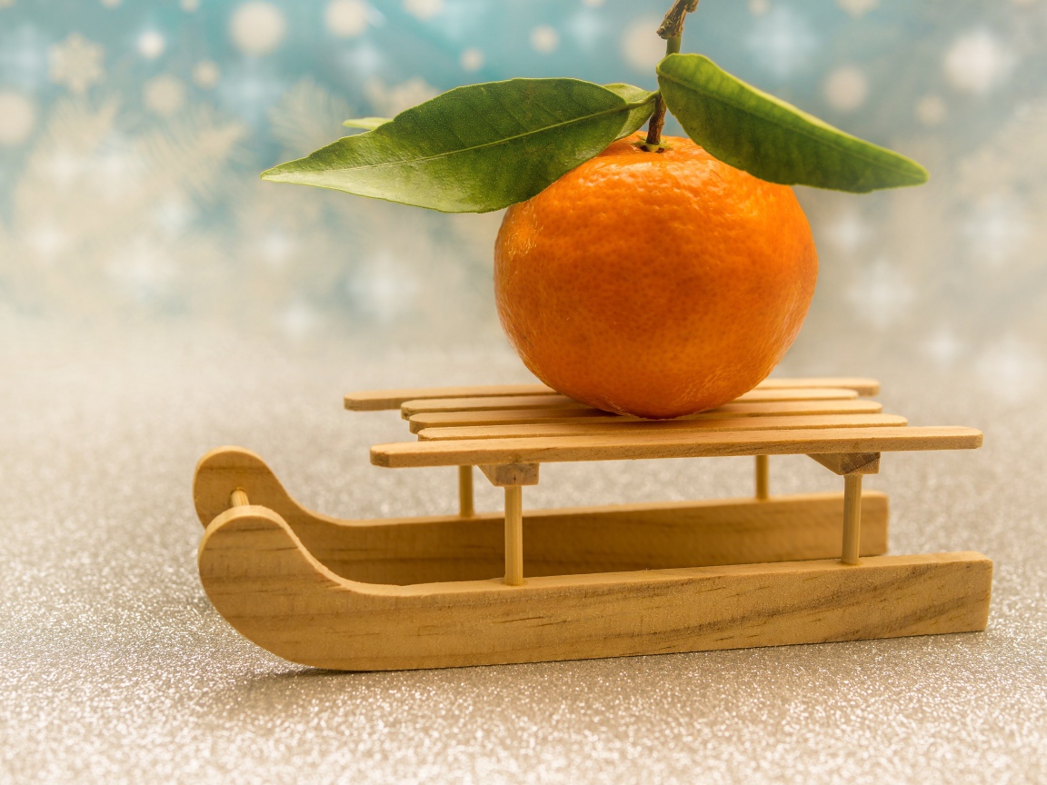 Большой оранжевый мандарин на маленьких санках