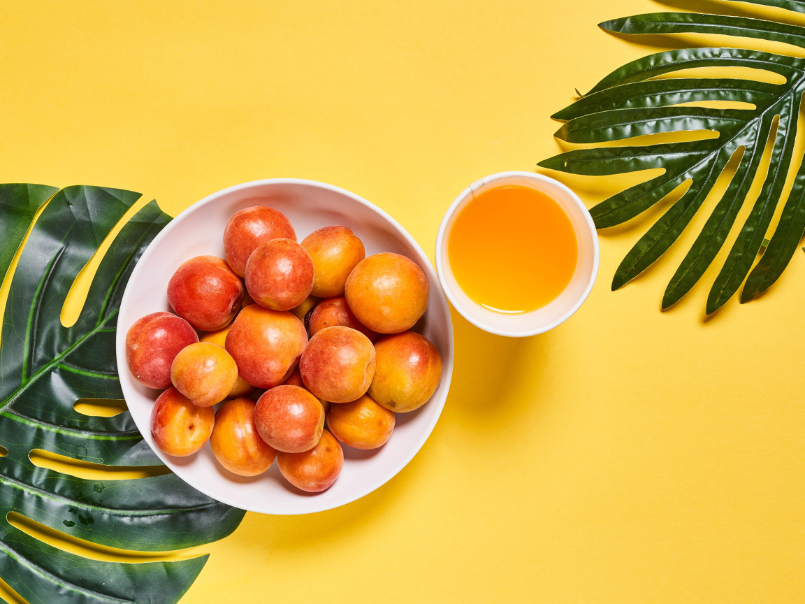 Вкусные спелые абрикосы с зелеными листьями на желтом фоне