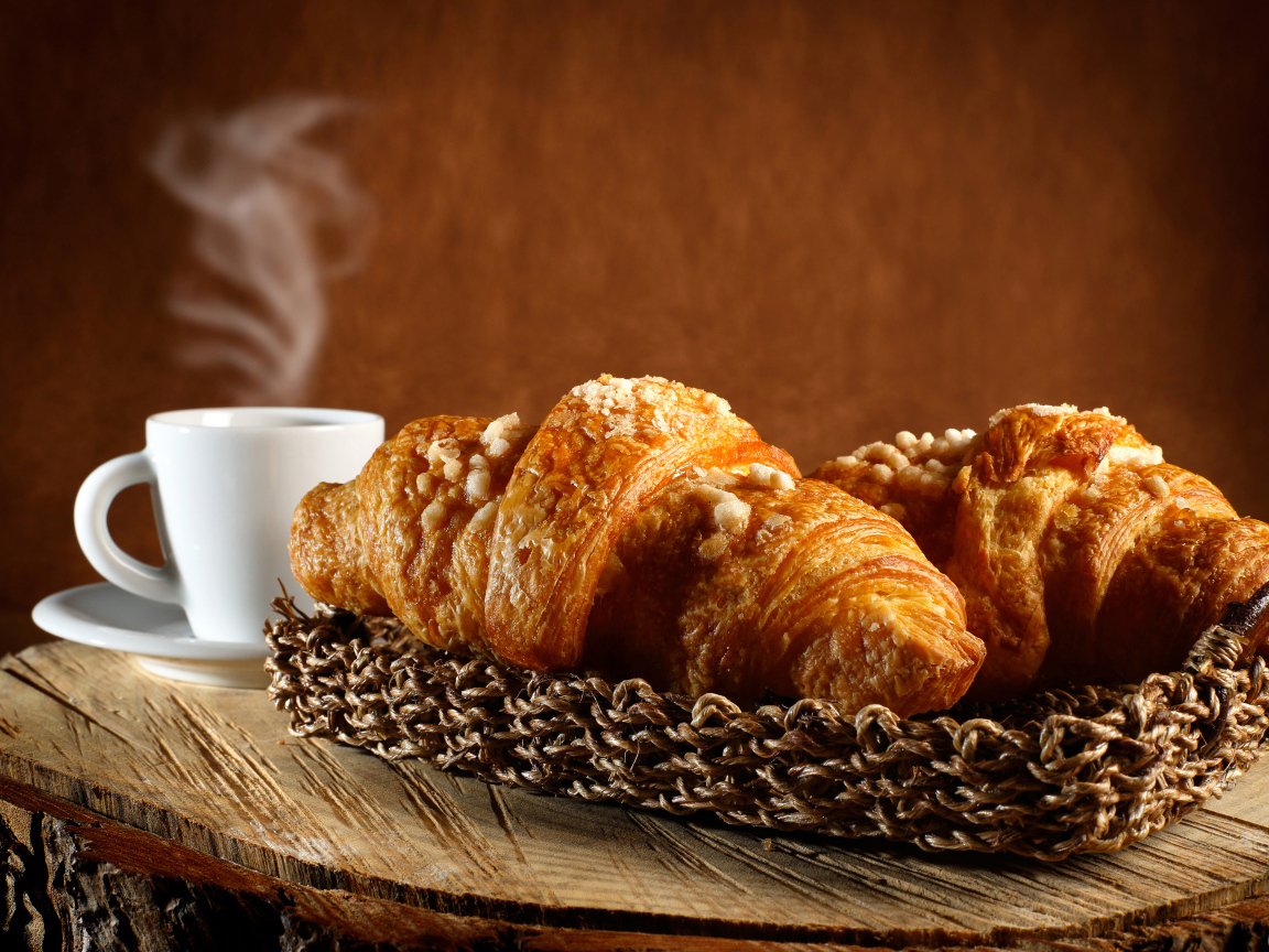 Два свежих круассана на столе с кофе 