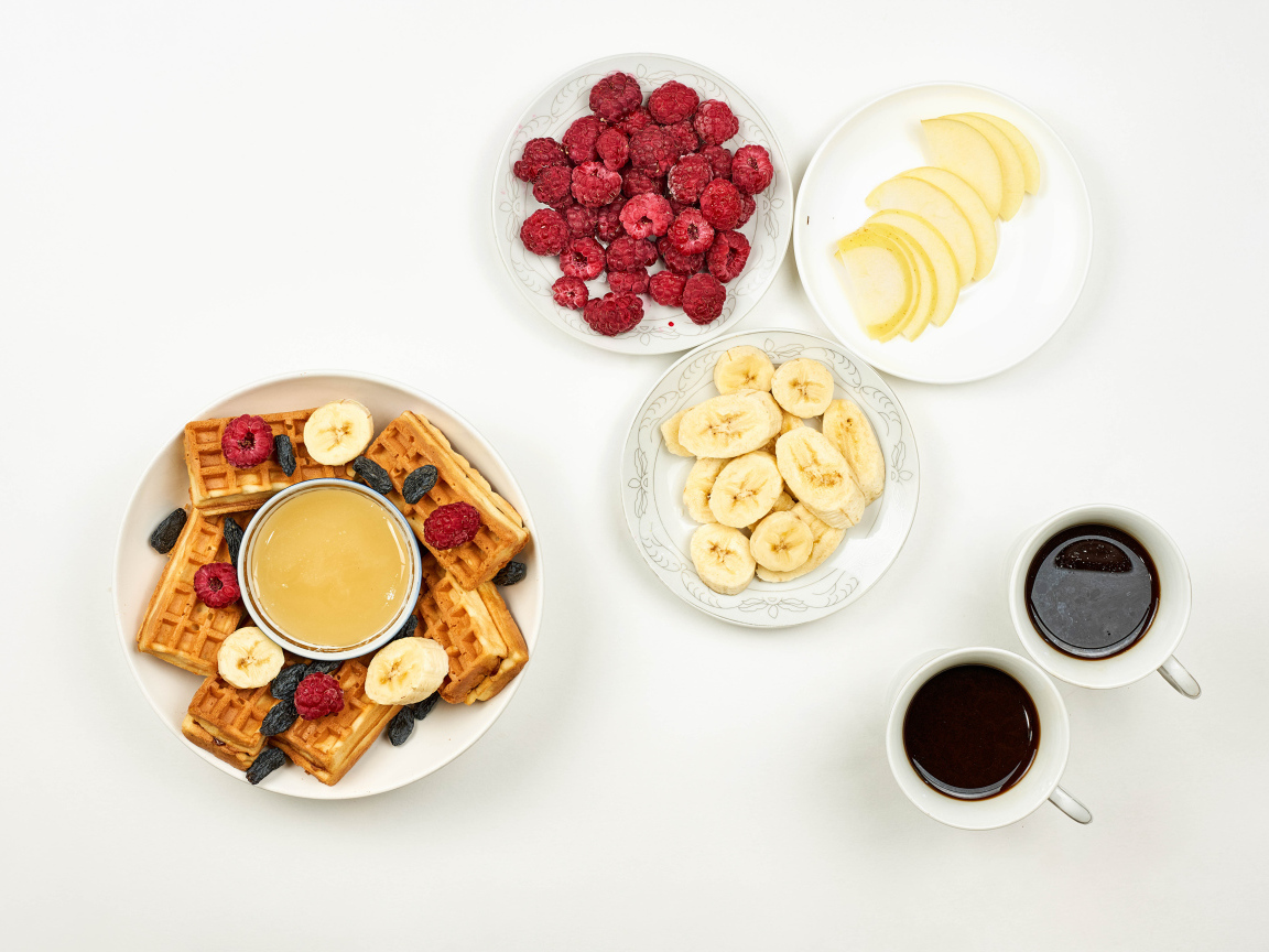 Сладкие вафли с малиной и бананами на столе  с кофе