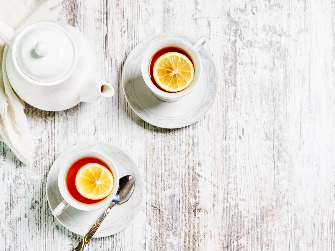 Две чашки чая с лимоном на столе с белым чайником