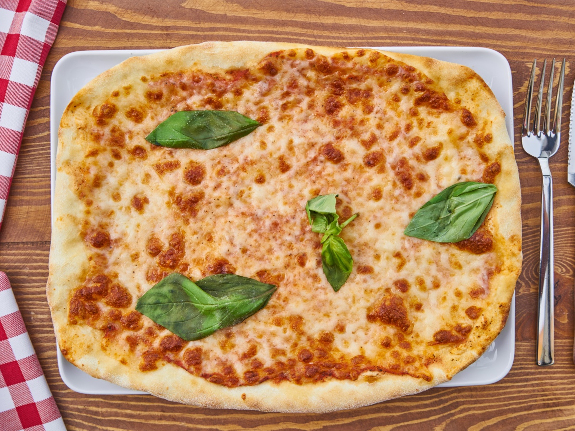 Пицца с сыром и листьями базилика на столе со столовыми приборами