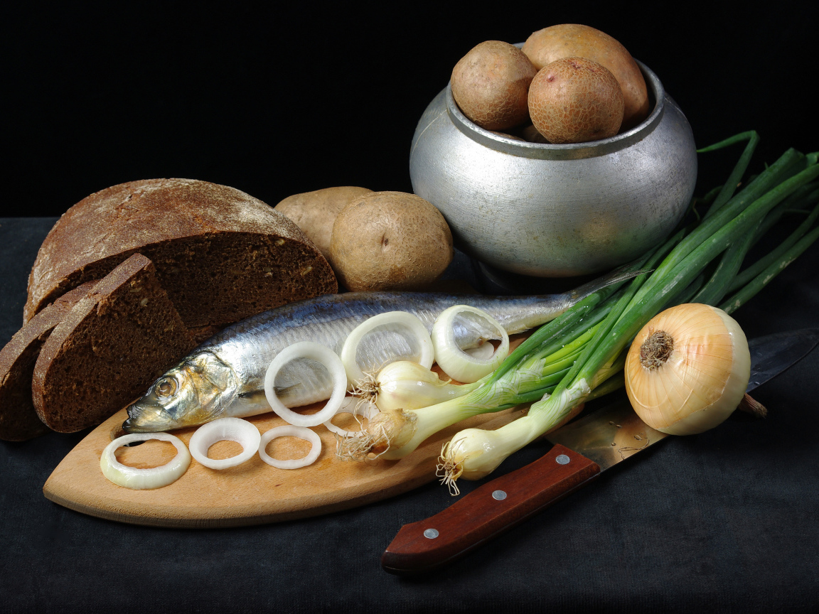 Сельдь на столе с картофелем, черным хлебом и луком 