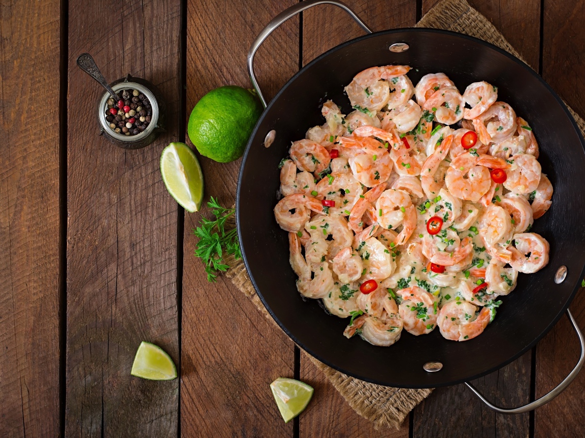 Креветки с соусом в сковороде на столе с лаймом