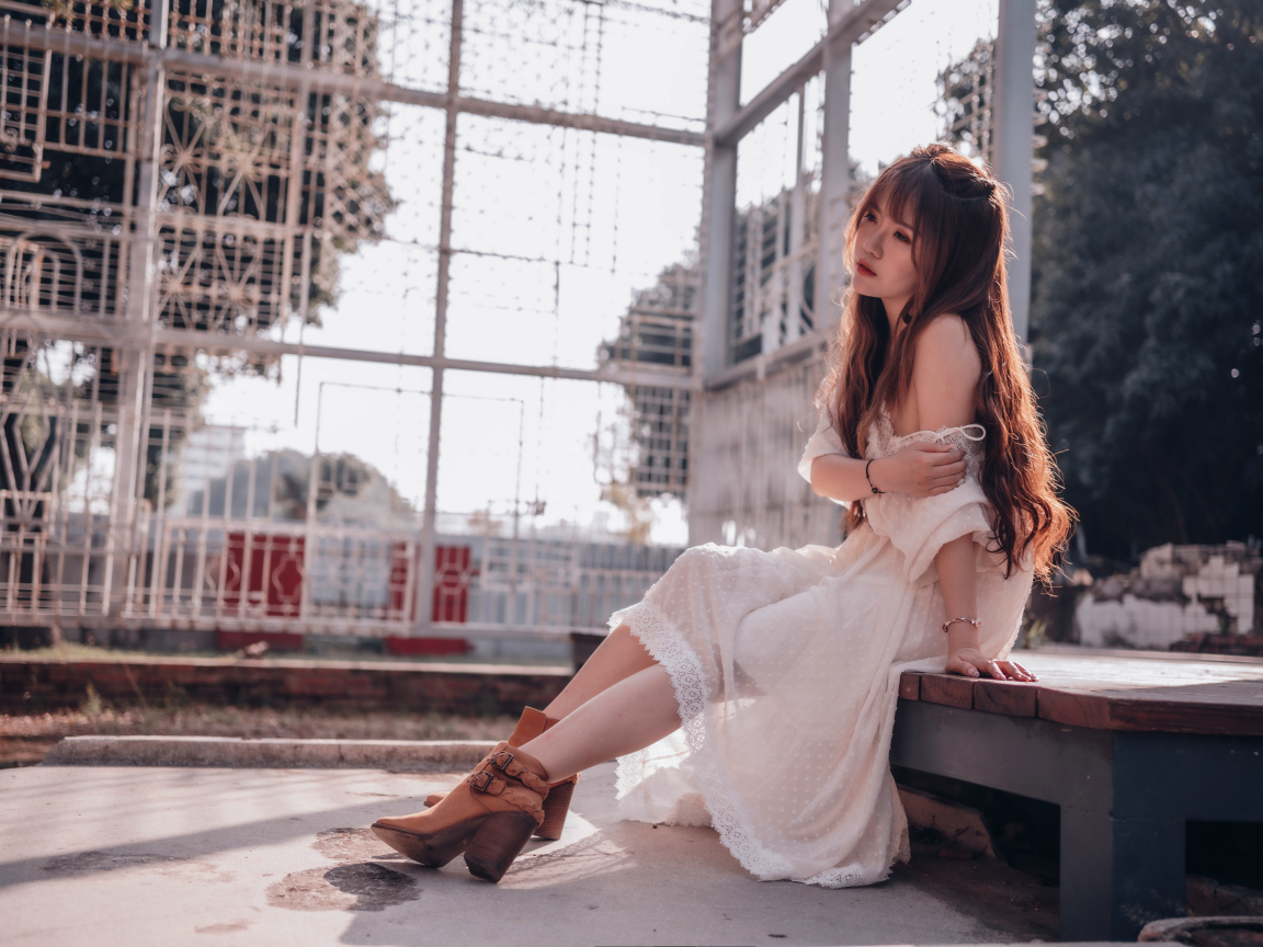 Красивая девушка азиатка в белом платье сидит на лавочке