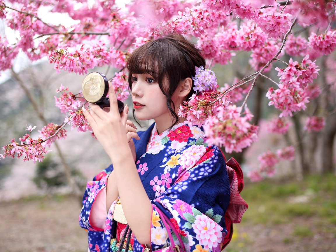Девушка в кимоно стоит у куста сакуры