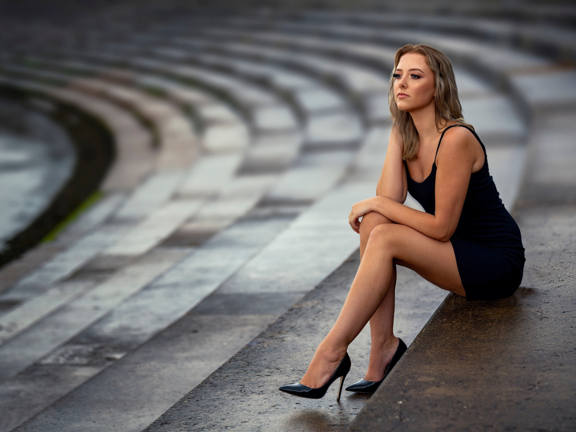 Девушка в коротком черном платье сидит на ступеньках