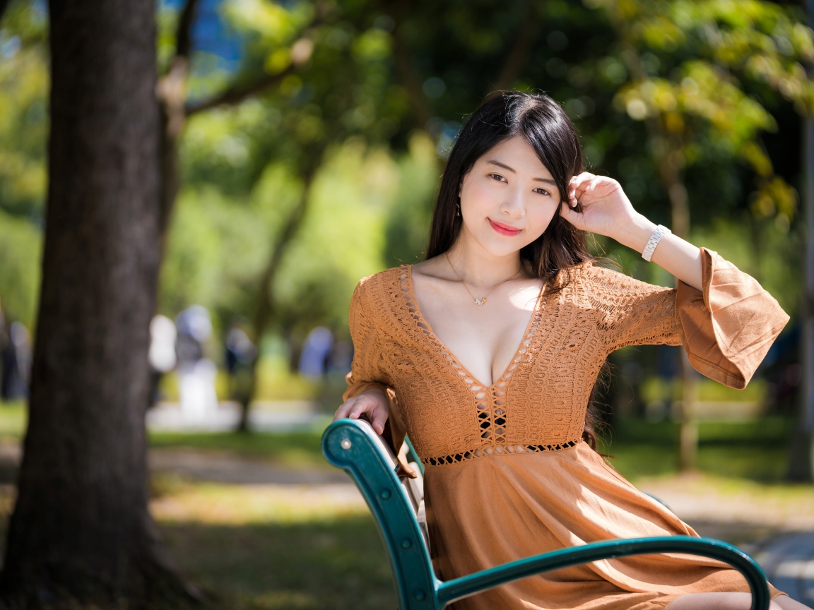 Молодая девушка азиатка в коричневом платье сидит на лавке