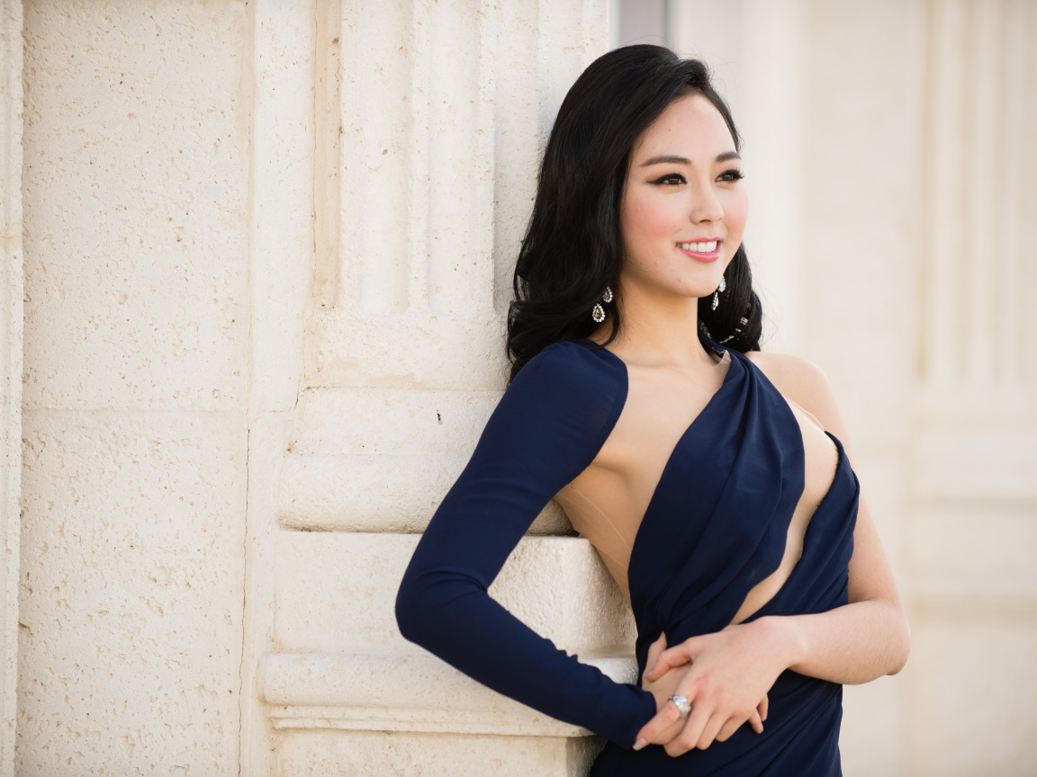 Молодая девушка в платье стоит у стены 