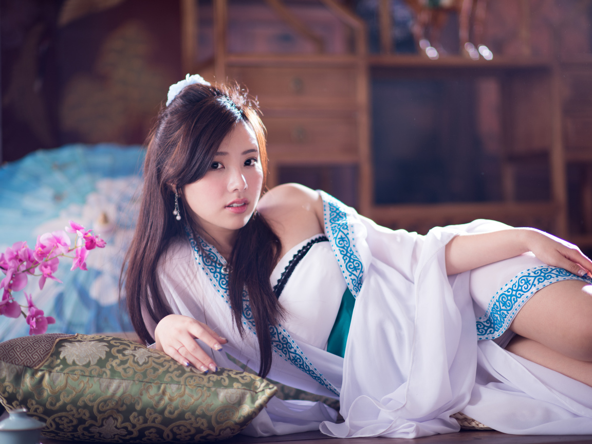 Девушка азиатка в красивом платье лежит на кровати 