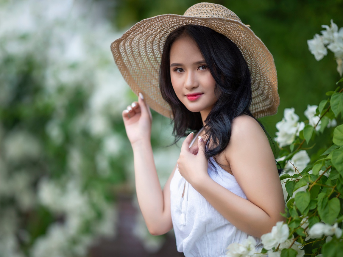 Девушка азиатка в большой шляпе у зеленого куста