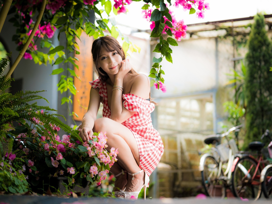 Девушка азиатка сидит на корточках у розового цветка